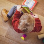 selective focus photography of sitting toddler in red sweater holding book